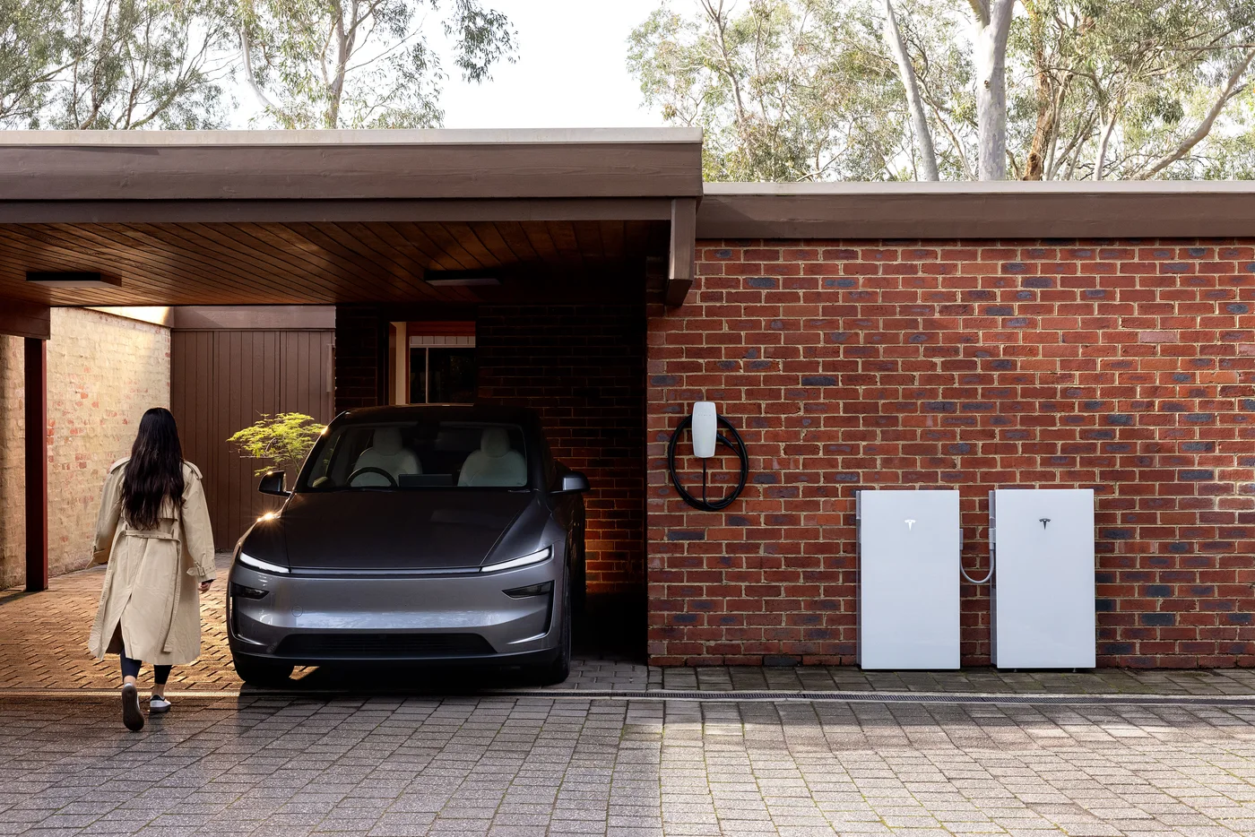 Tesla Powerwall units installed on a brick house beside an electric vehicle
